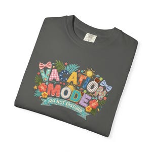 May include: Dark grey t-shirt featuring the embroidered phrase "VACATION MODE DO NOT DISTURB". The design incorporates colourful letters, tropical flowers, suns, and bows.