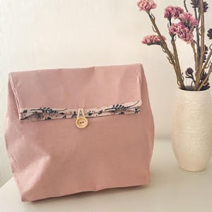 Peut inclure: Un sac de rangement en tissu rose avec une bordure à imprimé floral et une fermeture à bouton en bois.