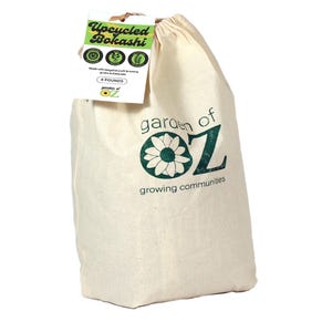 May include: A cream-colored canvas bag with the text "garden of OZ" in green, featuring a daisy design. A tag reads "Upcycled Bokashi" and "4 POUNDS". The bag is tied at the top with a natural fiber.