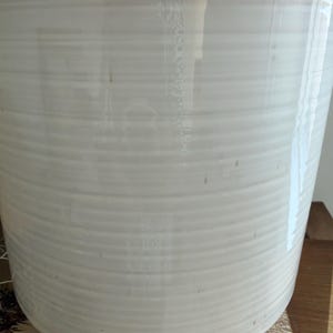 Peut inclure: Un pot de fleurs cylindrique en céramique avec une finition blanche brillante et une texture nervurée horizontale. Le bord présente un accent subtil brun clair ou beige, et la surface réfléchit la lumière, offrant un aspect émaillé lisse.