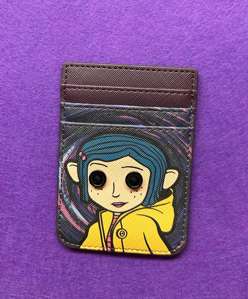 May include: A rectangular card holder featuring a cartoon character with blue hair and button eyes, wearing a yellow jacket. The card holder has a dark brown top section with card slots and a colorful swirling background.