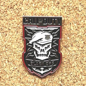 May include: A black, red, and white metal pin with the words "CALL OF DUTY" at the top and "BLACK OPS" at the bottom. The pin features a skull wearing a beret and a shield design.
