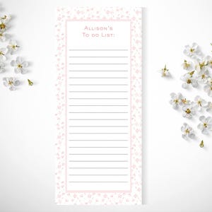 May include: A rectangular notepad with a light pink floral border and a white center. The top of the page features the text 'Allison's To do List:' in pink, followed by a series of horizontal black lines for writing tasks and notes.