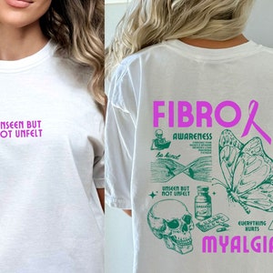 May include: White t-shirt with a pink ribbon and green text that reads "FIBRO AWARENESS" and "UNSEEN BUT NOT UNFELT". The text also includes "EVERYTHING HURTS MYALGIA".