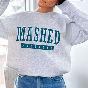 May include: A gray sweatshirt with the text "MASHED POTATOES" in blue lettering.