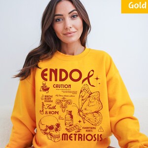 May include: Yellow sweatshirt with a red graphic design that says "ENDO & METRIOSIS" with a butterfly, skull, and pills. The graphic also includes the words "CAUTION", "WHOLE BODY DISEASE", "Courage", "Faith & HOPE", and "EVERYTHING HURTS".