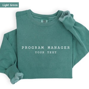 May include: Light green sweatshirt with the text "PROGRAM MANAGER YOUR TEXT" printed in white.