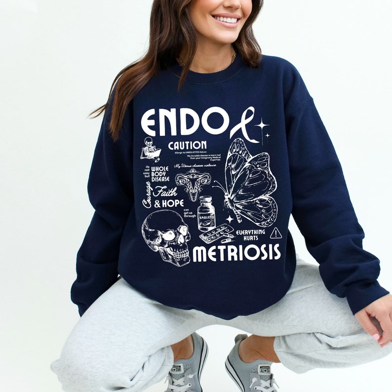 May include: Navy blue sweatshirt with a white graphic design that says "ENDO & METRIOSIS" with a skull, butterfly, and other medical illustrations. The text "CAUTION" is also included in the design.