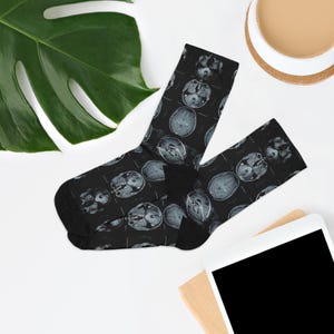 May include: Black socks with a repeating pattern of gray brain scan images. The socks are made of a soft material and are designed to fit most adult sizes. The socks are a unique and quirky accessory.