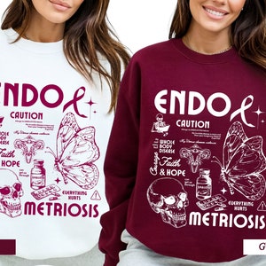 May include: Two sweatshirts, one white and one burgundy, with a graphic design featuring a butterfly, a skull, and the text "ENDOL CAUTION WHOLE BODY DISEASE Courage Faith & HOPE EVERYTHING HURTS METRIOSIS".