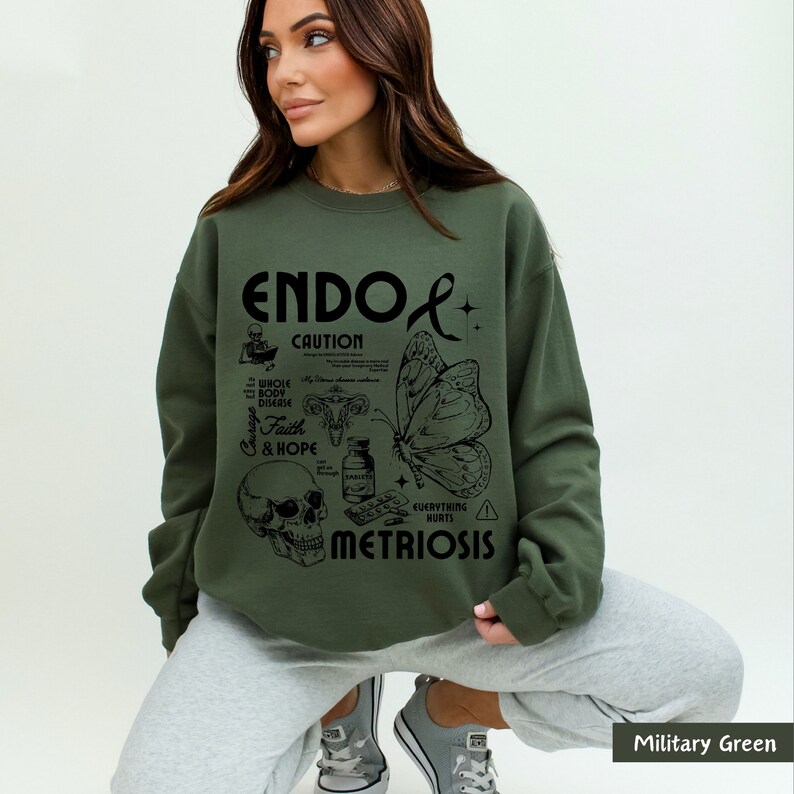 May include: A green sweatshirt with a black graphic design that says "ENDO CAUTION" and includes a butterfly, skull, and other medical symbols. The text "EVERYTHING HURTS" and "METRIOSIS" are also included in the design.