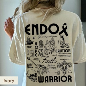 K&ouml;nnte beinhalten: Ein T-Shirt in Elfenbein mit einem schwarzen grafischen Design, das das Wort "Endo" und verschiedene Symbole im Zusammenhang mit Endometriose zeigt, darunter einen Schmetterling, einen Sch&auml;del, eine Geb&auml;rmutter und einen L&ouml;ffel. Der Text "You're not your diagnosis" und "Faith Warrior" ist ebenfalls im Design enthalten.