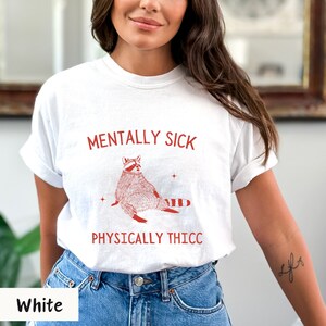 May include: White t-shirt with a red raccoon illustration and the text "Mentally Sick Physically Thicc".