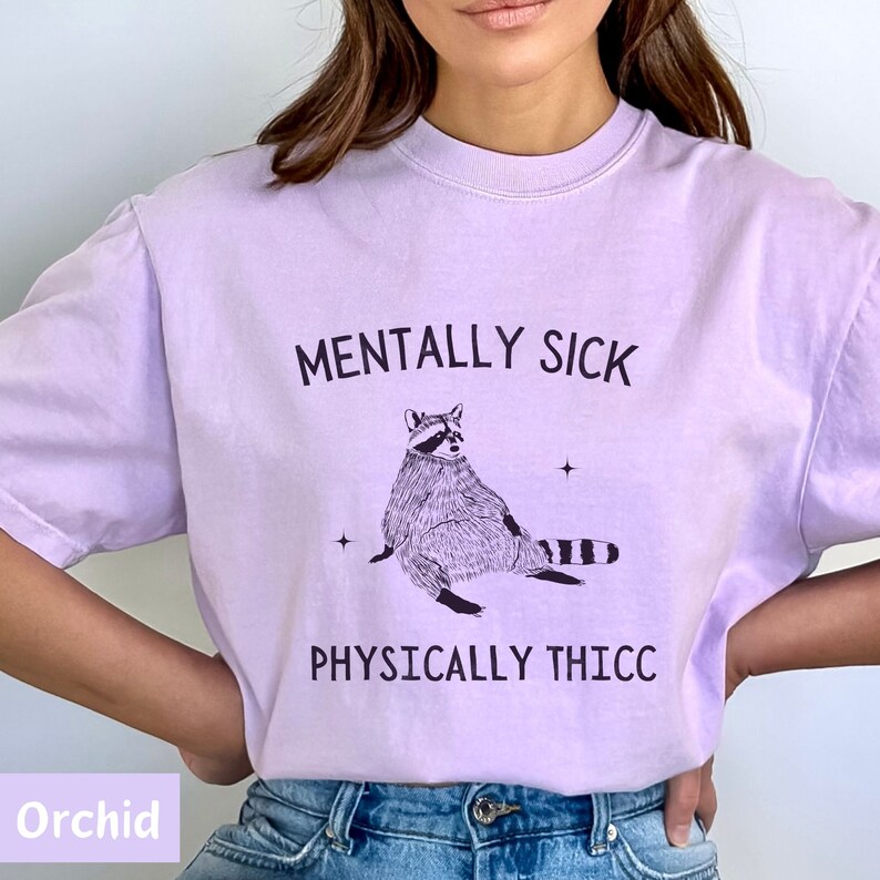 May include: A lavender t-shirt with a graphic of a raccoon and the text "Mentally Sick Physically Thicc".