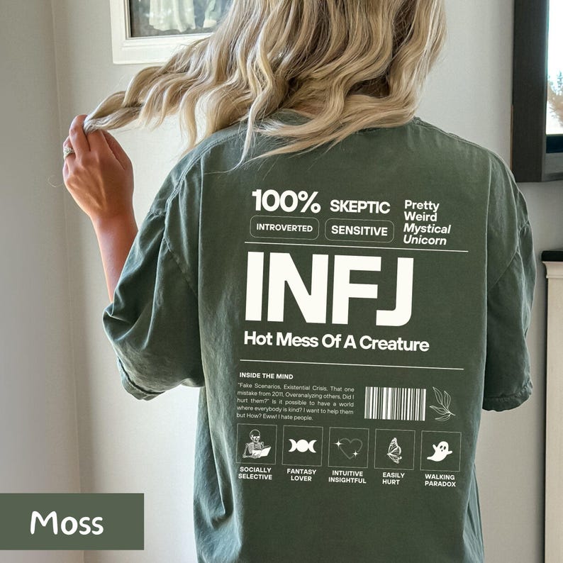 May include: A green t-shirt with white text that reads "100% Skeptic", "Introverted", "Sensitive", "Pretty Weird Mystical Unicorn", "INFJ", "Hot Mess Of A Creature", and "Inside The Mind". The text "Inside The Mind" is followed by a paragraph of text. Below the text are eight icons with text below each icon. The icons are a skull, a triple moon symbol, a heart, a butterfly, a ghost, a book, a flower, and a lightbulb. The text below the icons reads "Socially Selective", "Fantasy Lover", "Intuitive Insightful", "Easily Hurt", "Walking Paradox".