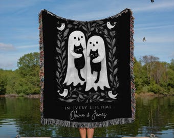 May include: Black woven throw blanket featuring a ghost couple each holding a black cat, surrounded by a floral design and small ghost illustrations. The text "IN EVERY LIFETIME" and names "Olivia & James" are printed on the blanket.