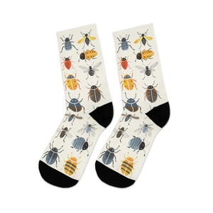 May include: A pair of white socks with a repeating pattern of colorful insects, including beetles, bees, and flies. The socks have black heels and toes. The insects are in shades of blue, yellow, orange, and black.