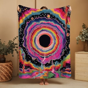 Puede incluir: Una manta rectangular con un dise&ntilde;o psicod&eacute;lico vibrante que presenta un gran c&iacute;rculo negro central rodeado por anillos conc&eacute;ntricos de colores brillantes rosa, naranja, amarillo, verde y azul, sobre un fondo de espacio oscuro y estrellado.