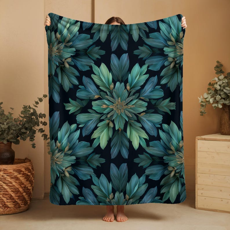 May include: A large, dark blue blanket with a symmetrical floral pattern in shades of teal and green. The design features stylized leaves arranged in a radial pattern. The blanket is held up, showcasing its size and design.