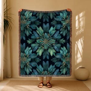 May include: A rectangular throw blanket with a dark navy background and a symmetrical pattern of teal and green leaves. The blanket has a fringed edge in a brown color.