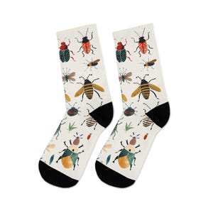 May include: A pair of white socks with a repeating pattern of colorful insects, including beetles, bees, and flies. The socks have black heels and toes. The insects are in shades of red, green, yellow, and brown.