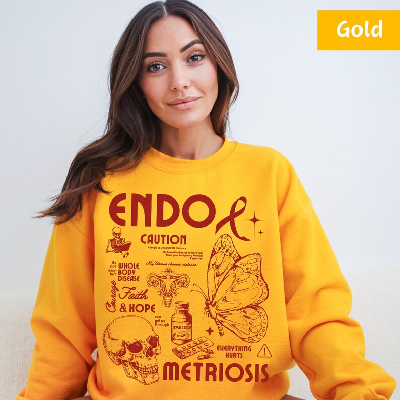 May include: Yellow sweatshirt with a red graphic design that says "ENDO & METRIOSIS" with a butterfly, skull, and pills. The graphic also includes the words "CAUTION", "WHOLE BODY DISEASE", "Courage", "Faith & HOPE", and "EVERYTHING HURTS".