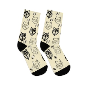 May include: A pair of socks with a cream-colored background and a repeating pattern of black and white wolf faces and claw marks. The socks have black heels and toes.