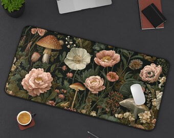 May include: A rectangular desk mat featuring a dark background with a floral and mushroom design. The design includes pink and white flowers, brown mushrooms, and green foliage. A computer mouse rests on the mat.