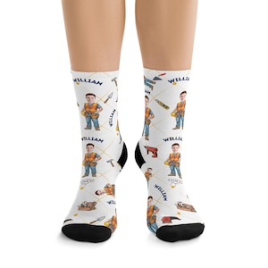 May include: White socks with a repeating pattern of a cartoon construction worker, tools, and the name "WILLIAM" in a handwritten style. The socks have black heels and toes.