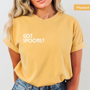 K&ouml;nnte beinhalten: Ein senfgelbes T-Shirt mit dem Aufdruck "GOT SPOONS?" in Wei&szlig; auf der Vorderseite.