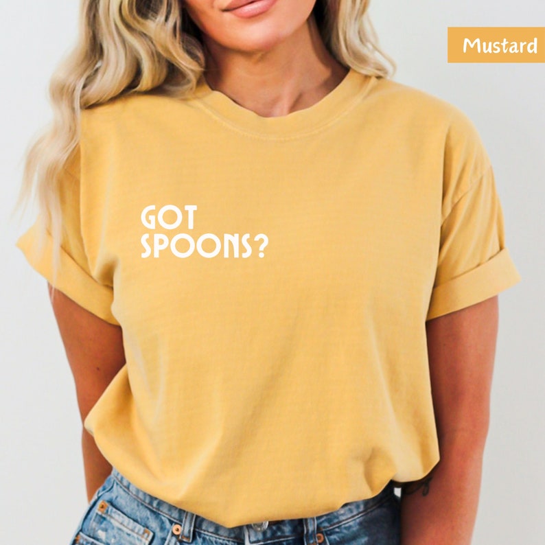 K&ouml;nnte beinhalten: Ein senfgelbes T-Shirt mit dem Aufdruck "GOT SPOONS?" in Wei&szlig; auf der Vorderseite.