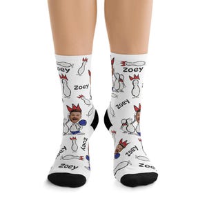 May include: White socks with a repeating pattern of cartoon bowling pins, a person's face, and the name "Zoey". The socks have black heels and toes. The bowling pins are wearing crowns.