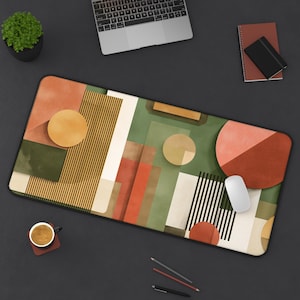 Puede incluir: Alfombrilla de escritorio rectangular con un diseño geométrico abstracto en tonos verdes, naranjas y beige. El diseño incluye círculos, rectángulos y rayas verticales. Un ratón de ordenador blanco descansa sobre la alfombrilla.