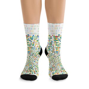 May include: A pair of crew socks with a colorful geometric pattern. The socks feature a white background with a design of small, multi-colored rectangles arranged in a circular pattern. The toes and heels are black.