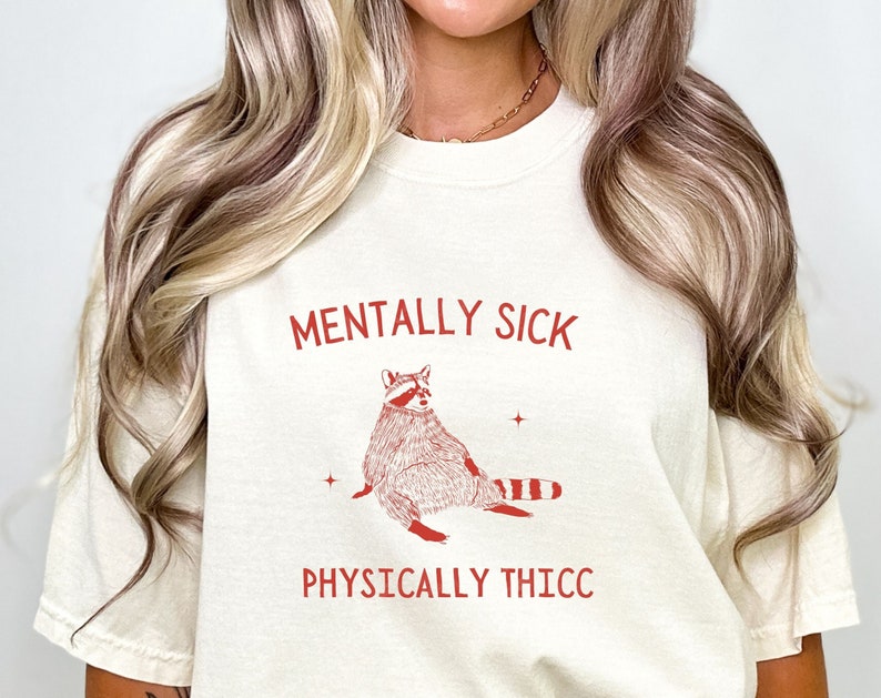 May include: A white t-shirt with red text that reads "Mentally Sick" and "Physically Thicc". A cartoon raccoon is printed in red on the shirt.