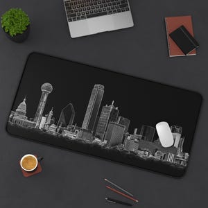 May include: Black rectangular desk mat featuring a white line drawing of the Dallas, Texas skyline. Includes the Reunion Tower, skyscrapers, and other buildings. A white computer mouse is on the right side of the mat.