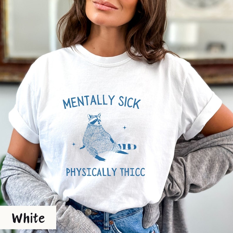 May include: White t-shirt with a blue raccoon illustration and the text "Mentally Sick Physically Thicc".