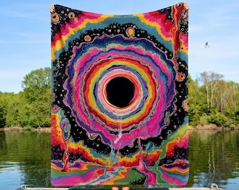 May include: A rectangular throw blanket featuring a vibrant, psychedelic design with a large black circular center surrounded by concentric rings of bright pink, orange, yellow, green, and blue colors, set against a dark, starry space background.