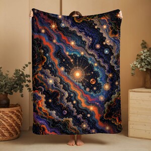 May include: A large, rectangular blanket featuring a vibrant, abstract design reminiscent of a nebula or galaxy. The design incorporates swirling patterns in shades of blue, orange, and gold, with numerous star-like accents. The blanket is held up by a person.