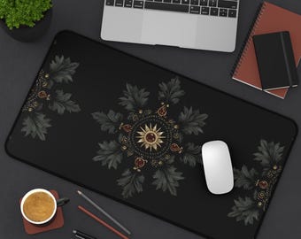 Puede incluir: Alfombrilla de escritorio negra con un diseño floral decorativo en dorado y verde oscuro. El diseño presenta un sol central con detalles rojos y patrones de hojas ornamentadas. Un ratón blanco está sobre la alfombrilla.
