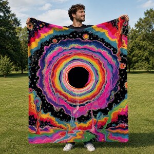 Puede incluir: Una manta rectangular con un dise&ntilde;o psicod&eacute;lico vibrante que presenta un gran c&iacute;rculo negro central rodeado de anillos conc&eacute;ntricos de colores brillantes del arco&iacute;ris, incluyendo rosa, naranja, amarillo y azul, sobre un fondo oscuro.