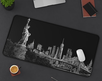 Könnte beinhalten: Schwarze rechteckige Schreibtischunterlage mit einer weißen Skizze der Skyline von New York City, einschließlich der Freiheitsstatue, Wolkenkratzern und der Brooklyn Bridge. Eine weiße Computermaus liegt auf der Matte.