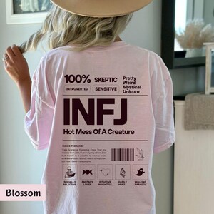May include: Pink t-shirt with the text "100% Skeptic", "Introverted", "Sensitive", "Pretty Weird Mystical Unicorn", "INFJ", "Hot Mess Of A Creature", and "Inside The Mind". The shirt also has a graphic with five icons representing "Socially Selective", "Fantasy Lover", "Intuitive Insightful", "Easily Hurt", and "Walking Paradox".