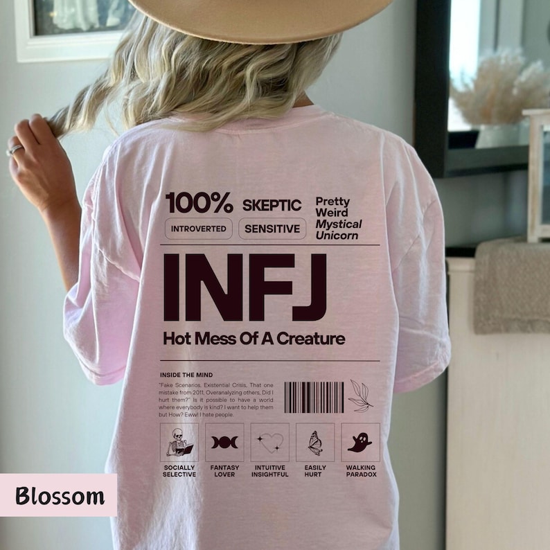 May include: Pink t-shirt with the text "100% Skeptic", "Introverted", "Sensitive", "Pretty Weird Mystical Unicorn", "INFJ", "Hot Mess Of A Creature", and "Inside The Mind". The shirt also has a graphic with five icons representing "Socially Selective", "Fantasy Lover", "Intuitive Insightful", "Easily Hurt", and "Walking Paradox".