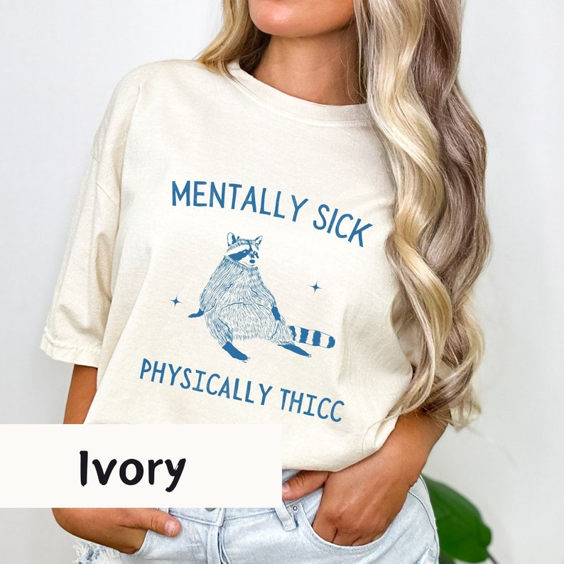 May include: Ivory t-shirt with a blue raccoon graphic and the text "Mentally Sick Physically Thicc".