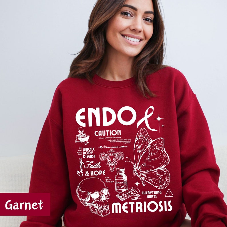 May include: Red sweatshirt with a white graphic design that says "ENDO+ CAUTION WHOLE BODY DISEASE Courage Faith & HOPE EVERYTHING HURTS METRIOSIS". The graphic also includes a skull, a butterfly, a uterus, and pills.