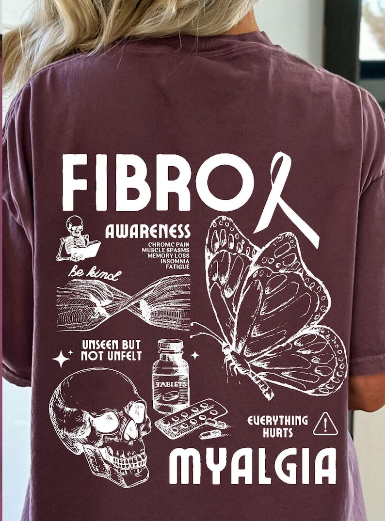 May include: A maroon t-shirt with a white graphic design featuring a butterfly, a skull, pills, and the text "FIBRO AWARENESS" and "MYALGIA". The text "Be kind" and "UNSEEN BUT NOT UNFELT" are also included in the design.