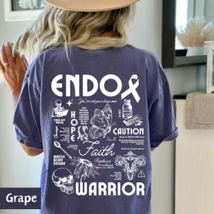 K&ouml;nnte beinhalten: Lilafarbenes T-Shirt mit einem wei&szlig;en Grafikdesign, auf dem "Endox" steht und das einen Schmetterling, einen Sch&auml;del, eine Geb&auml;rmutter und andere Illustrationen enth&auml;lt. Der Text enth&auml;lt auch die W&ouml;rter "Hope", "Faith", "Warrior" und "Caution".