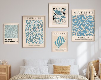 Op de afbeelding: Een slaapkamerinterieur met een wit bed, een rieten stoel en een dressoir. De muur is versierd met vijf ingelijste kunstprints met abstracte ontwerpen in blauw en wit. De prints zijn getiteld "Yayoi Kusama", "Paul Klee", "Henri Matisse", "Henri Matisse" en "Henri Matisse".