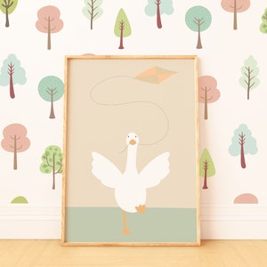 A nursery print featuring a white goose flying a kite, displayed against a pastel tree-patterned wallpaper. The framed print adds a whimsical touch to the room with its simple design and calming colors.
